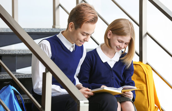 Cute boy and girl in school uniform sitting on stairs and reading book