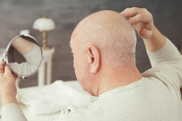 Senior bald man looking in mirror at home