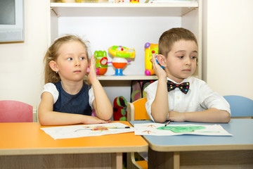 Adorable children boy and girl draws a brush and paints in nursery room. Kid in kindergarten in Montessori preschool class.