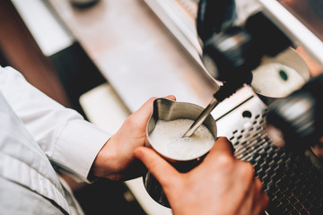 Professional bartender warming milk for cappuccino. Barista using coffee machine for latte art macchiato. Toned image