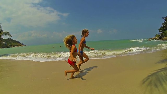 Two little girls running on the sea beach, slow motion