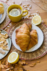 Black tea with lemon in yellow mug with croissants, buns and homemade cookies on wooden table