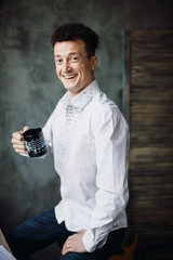 Happy man sits straight holding black cup with notes painted on it