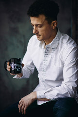 Curly man in white shirt sits with black cup and notes on it