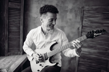 Obraz premium Happy man looks at neck of his electric guitar while he plays on it