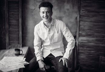 Black and white portrait of handsome man sitting at table with sheets of music on it