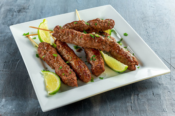 Homemade Kofta kebabs on skewers with lime and parsley on white plate