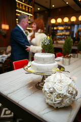 White bouquet and wedding cake stand on table before old wedding couple