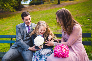 Man and woman in pink play with little girl sitting on blue bench