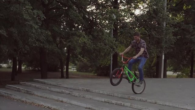 Ryder in the park by special BMX bicycle makes a jump through steps and scrolls a frame by 360 degrees.