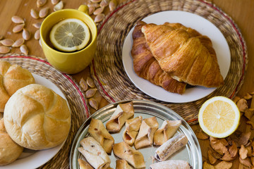 Black tea with lemon in yellow mug with croissants, buns and homemade cookies on wooden table