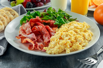 Morning Scrambled egg, bacon breakfast with orange juice, milk, fruit, bread on white plate