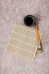 Bamboo mat for cooking sushi, soy sauce and chopsticks on a gray stone background