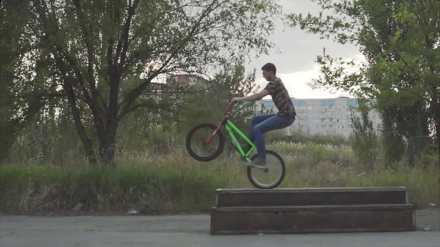 The slow movement of the guy jumping on stage, which is in the skate park, doing a quick slide to the rear wheel of bicycle BMX, then jumps down on asphalt, carrying air around the scroll wheel frame.