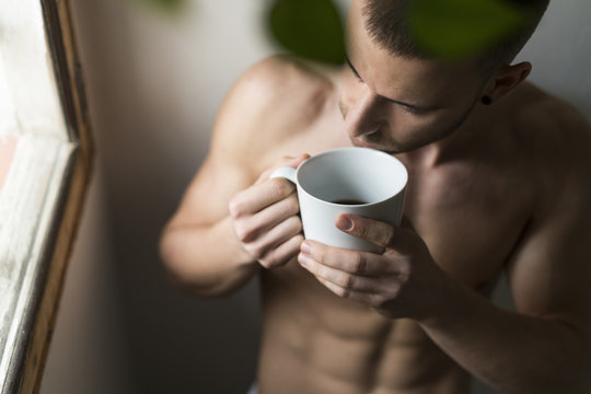 Attractive young man with six pack drinking coffee
