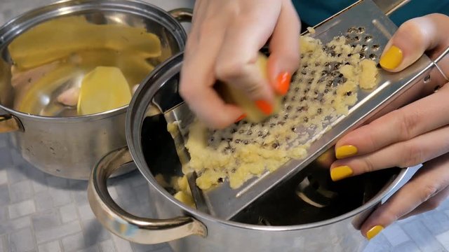 Women hands with a grater grate the potatoes in the kitchen.