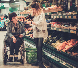 Young girl helping her disabled mothter in wheelchair in a grocery store