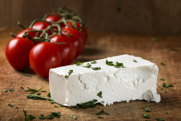 Feta cheese with bunch of cherry tomatoes in background on wood