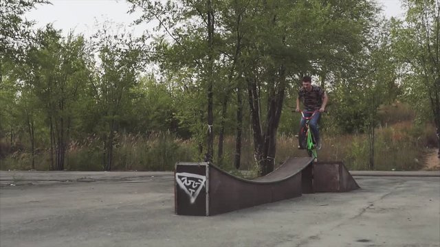 Ryder by special bicycle jumps through an obstacle and lands on a plain surface in the summer skatepark.