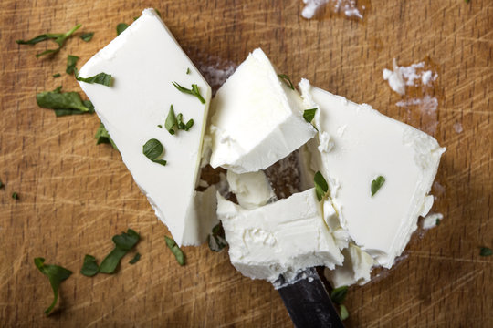 Feta cheese pieces with knife and herbs on wood