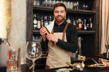 Happy young bearded man bartender standing in cafe.