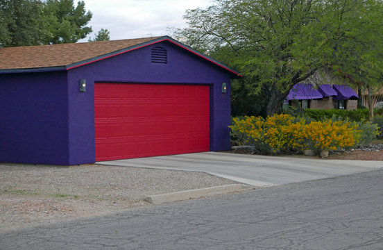 Violett gestrichene Garage mit rotem Rolltor und gelb bluehendem Busch in den USA