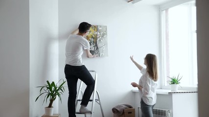 Moving house: Couple hanging picture on wall in new home