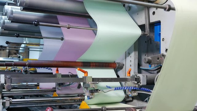 Blue, pink, green and yellow paper rolls on the assembly line of an envelope factory