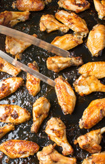 Cooking tongs holding bbq chicken wings