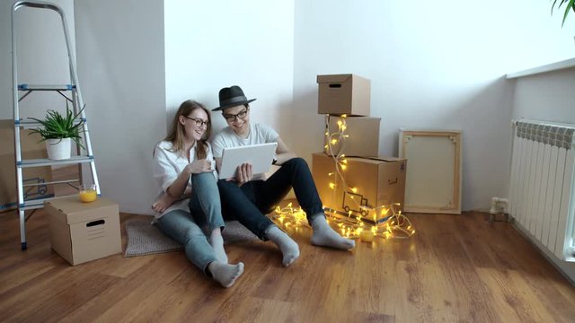 Young couple moving in new home.Sitting on floor and relaxing after cleaning and unpacking.Using tablet.