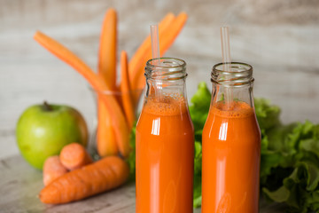 Fresh carrot juice in bottles on a grey wooden table