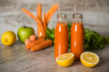 Fresh carrot juice in bottles on a grey wooden table