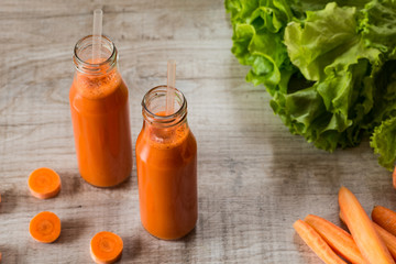 Fresh carrot juice in bottles on a grey wooden table