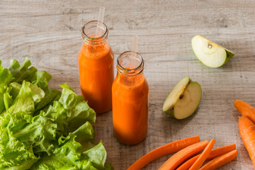 Fresh carrot juice in bottles on a grey wooden table