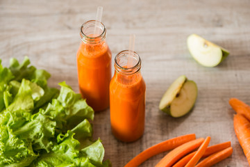 Fresh carrot juice in bottles on a grey wooden table