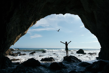 Silhouette of woman in mouth of cave standing on rock