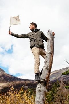 Man standing on tree trunk holding flag