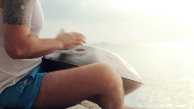 Man playing hang drum sitting on the stone at tropical beach, sound included. close up