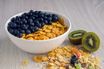 granola with blueberries in white bowl on wooden white background