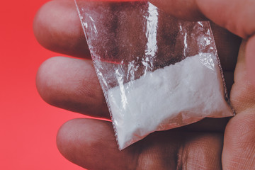Mans hand holding or giving, selling on palm plastic packet with cocaine powder 