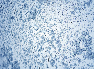 Snow and drops on blue toned car glass with blur effect.