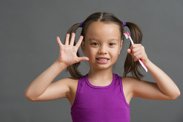Kid showing five while holding a toothbrush