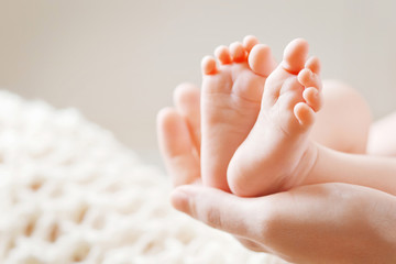 Baby feet in mother hands. Tiny Newborn Baby's feet on female Shaped hands closeup. Mom and her Child. Happy Family concept. Beautiful conceptual image of Maternity - obrazy, fototapety, plakaty