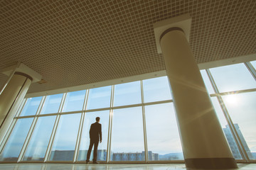 The businessman stand near panoramic window on background of sunlight