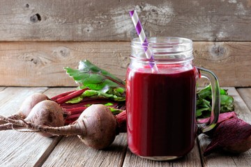 Fresh beet juice in a mason jar glass with beets over a rustic wood background