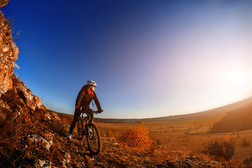 Wide angle view of cyclist standing with mountain bike on trail at sunrise