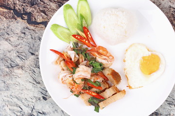 Thai food ,Jasmine rice topped stir - fried spicy basil with shrimp ,squid and crispy pork and heart shape of fried egg call Kao Pad Kra Prao Seafood.
