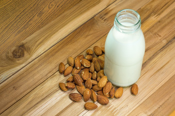 Almond milk in bottle glass with almonds on woodene background with copy space