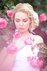  Beautiful Blond Bride near a Flowering Bush Roses Posing in a Wedding Dress