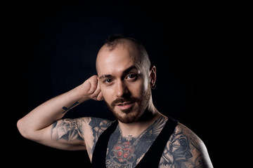 Obraz premium Close up portrait of brutal man with tattooed body on black background in black t-shirt. Attractive guy with naked torso look to the camera.